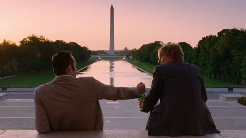 Two men sit beside the reflecting pool, facing the Washington Monument at sunset