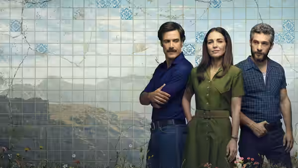 A woman in green stands between two men before a tiled landscape mural
