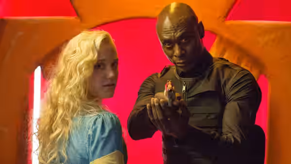 Major Carver (Lance Reddick) aims a gun beside a blonde young woman