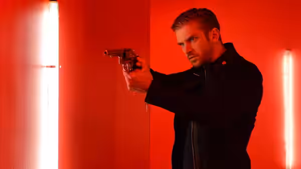 David (Dan Stevens) aims a handgun in a red-lit corridor