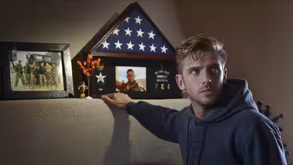 David (Dan Stevens) gestures toward a folded flag and military memorial