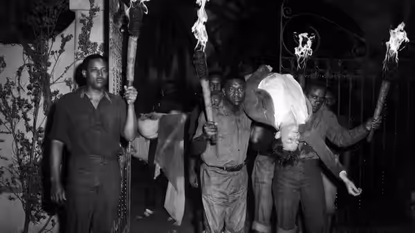 Men carry a limp woman upside down through a doorway with flaming torches