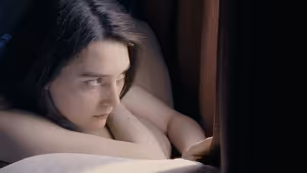 Autumn (Sidney Flanigan) lies in bed, peering past a curtain