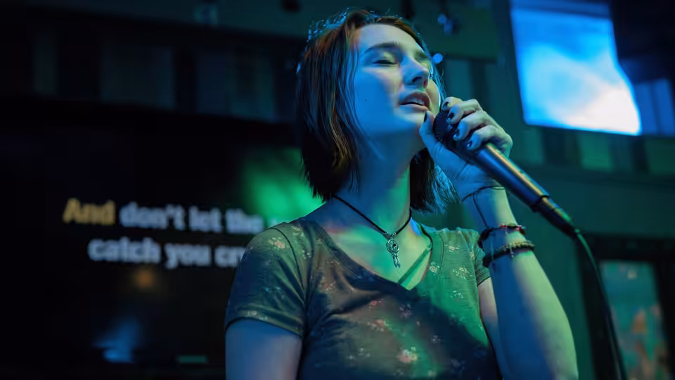 A young woman sings into a microphone on a dimly lit stage