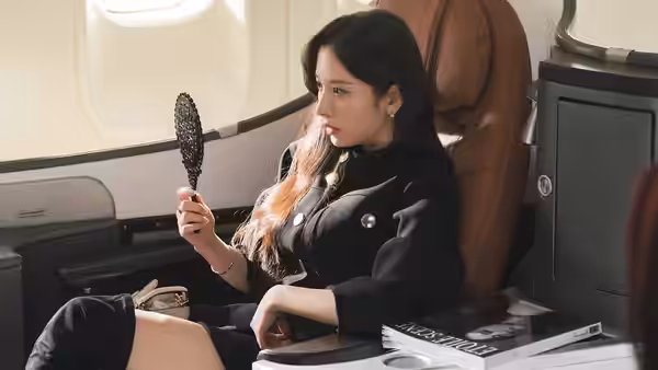Woman in black suit checks her reflection with a mirror on a private jet