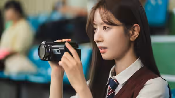 Young woman in school uniform holds a camcorder while seated indoors
