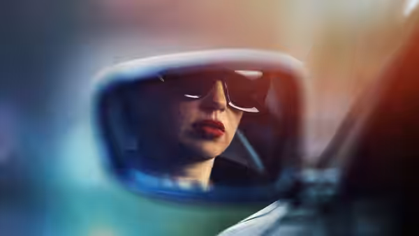 Woman wearing sunglasses reflected in a car's rearview mirror