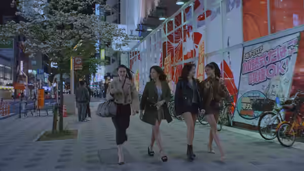 Four women walking along a neon-lit city street at night