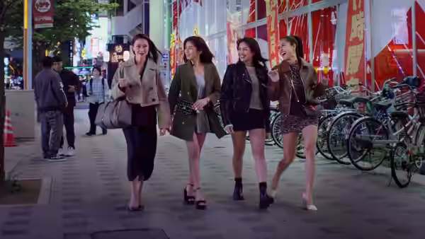 Four women walking together on a neon-lit city street at night