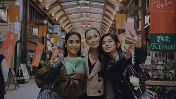 Three women taking selfies together inside a bustling shopping arcade