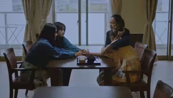 Three women holding hands across a wooden table in a bright room