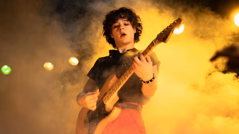 Musician with curly hair plays electric guitar on smoky stage