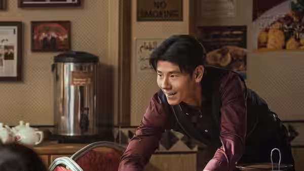 A young man leans across a counter in a small café