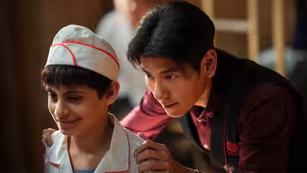 Man in vest places hand on shoulder of young boy in chef hat