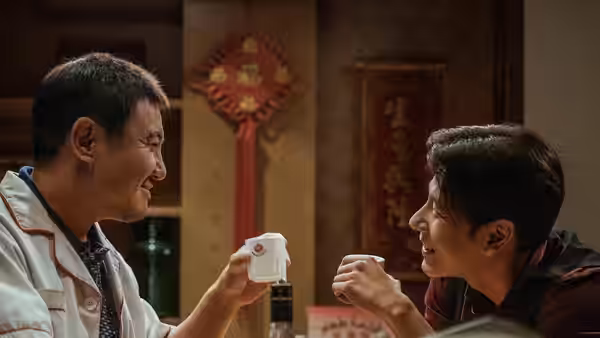 Two men smile at each other while holding small white cups in a restaurant