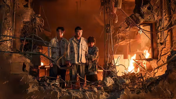 Three men stand amid rubble in a firelit ruined interior