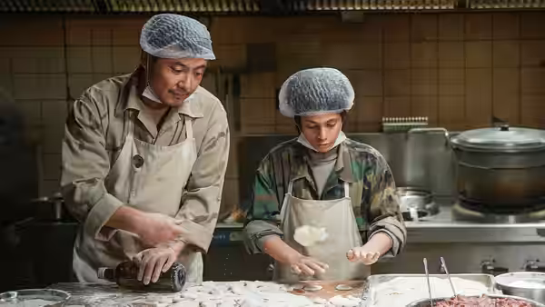 Two cooks prepare dough on a kitchen counter with various ingredients
