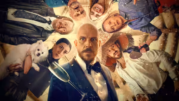 Filip (Gustaf Skarsgård) and party guests look down around a table with champagne and a dog