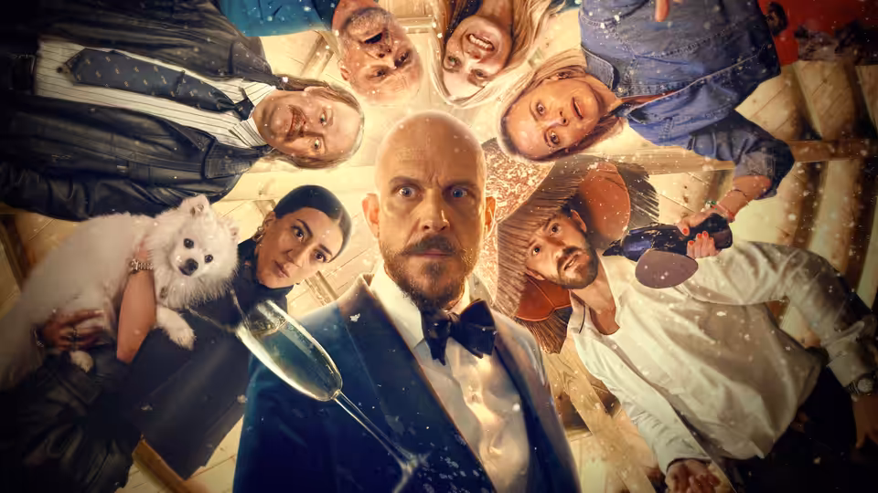 Filip (Gustaf Skarsgård) and party guests look down around a table with champagne and a dog