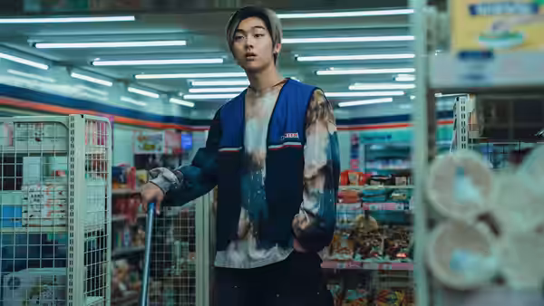 A young man in a blue work vest pushes a cart through a brightly lit market