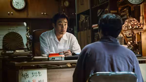 A man behind a counter speaks with a seated customer