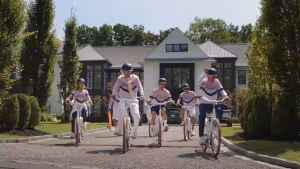 Four cyclists in matching outfits riding down a suburban driveway