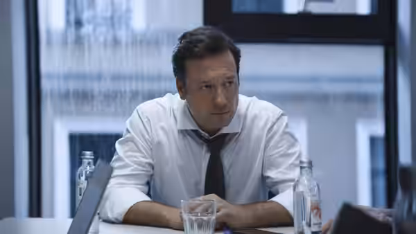 A man in a white shirt and tie seated at a conference table