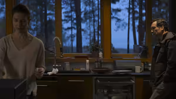 A woman standing in a kitchen while a man watches her