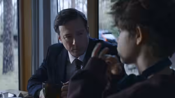 A man in a suit speaking with a young boy at a table