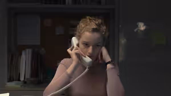 Jane (Julia Garner) talks on a corded phone at her desk in a dim office
