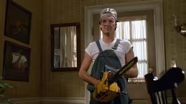 Jack (Michael Keaton) stands in overalls holding a power saw in a wallpapered room