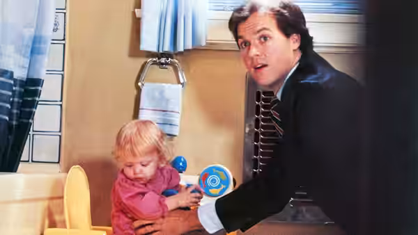 Jack (Michael Keaton) kneels beside a toddler in a bathroom, holding a toy