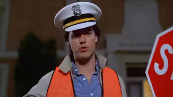 Jack (Michael Keaton) wears a traffic guard's cap and orange vest beside a stop sign