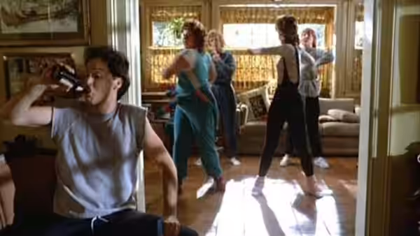 Jack (Michael Keaton) drinks from a bottle while women exercise in the living room