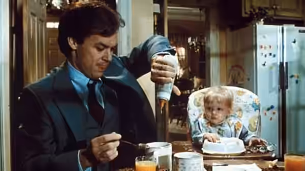 Jack (Michael Keaton) feeds breakfast to a baby at the kitchen table