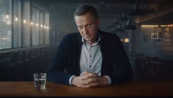 Alexei Navalny sits at a restaurant table, hands clasped and looking toward the camera