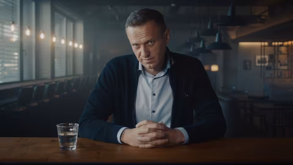 Alexei Navalny sits at a restaurant table, hands clasped and looking toward the camera