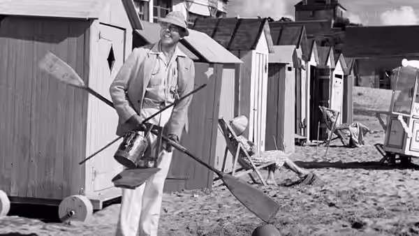 Monsieur Hulot (Jacques Tati) carries beach gear between the changing huts