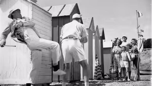 A man stretches beside a beach hut as holidaymakers watch