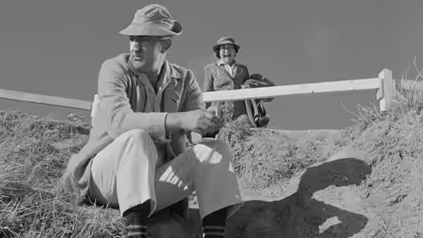 A seated man holds a beach rail while another man stands behind him