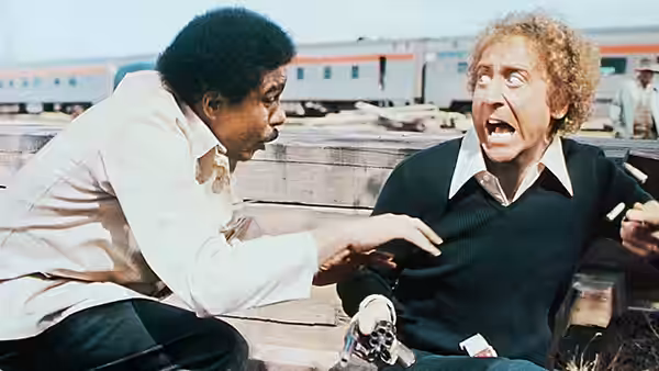 Grover Muldoon reaches toward George Caldwell beside a train platform