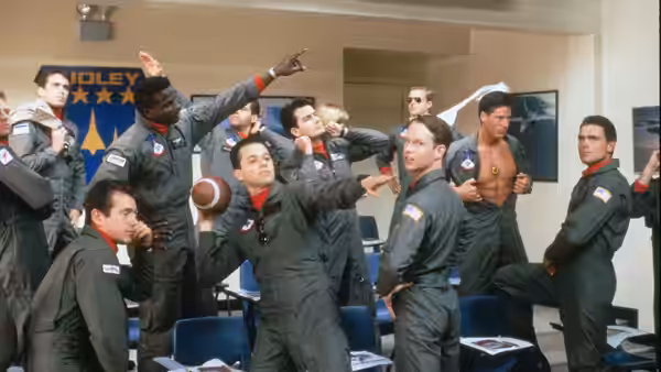 Naval aviators in flight suits strike playful poses in a squadron room