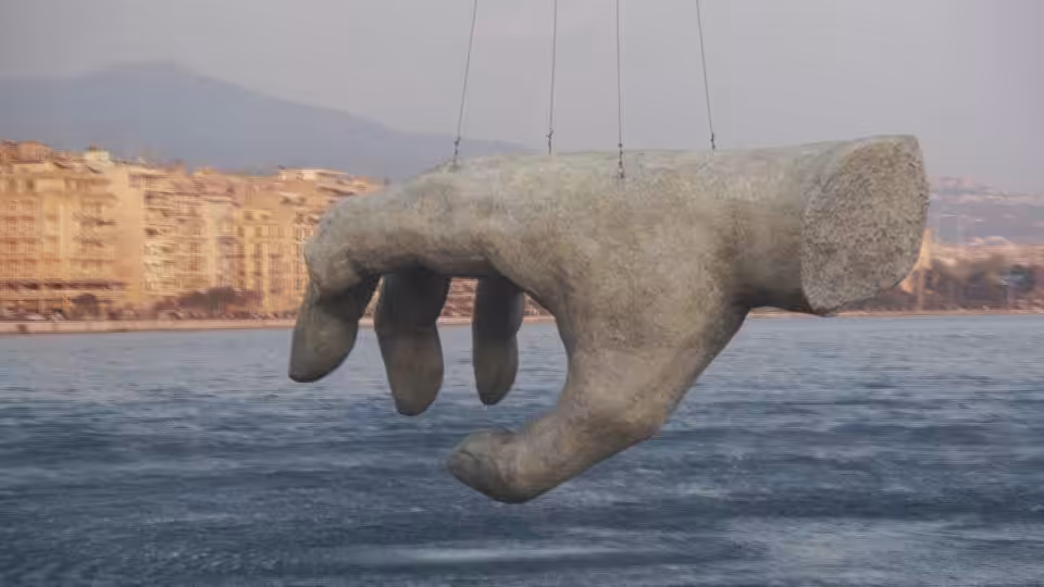 A giant stone hand hangs above the water near a coastal city