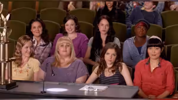 Beca Mitchell (Anna Kendrick) seated at a table with other women in an auditorium
