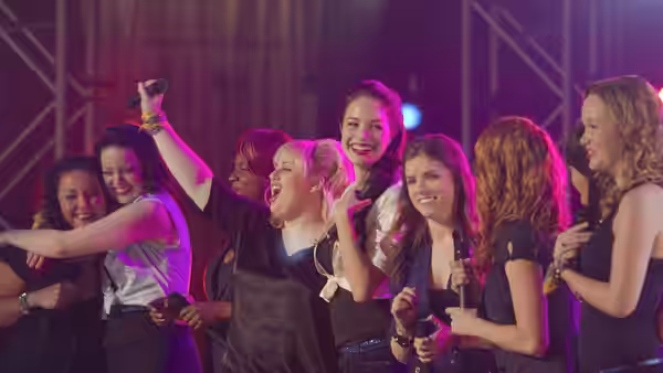 Group of women singing energetically on stage with microphones under colorful lights