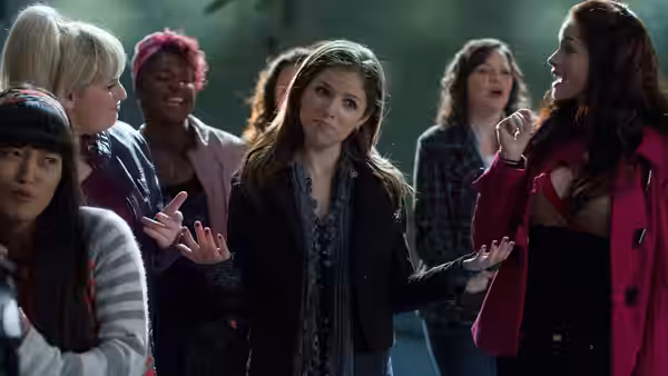 Beca Mitchell (Anna Kendrick) gesturing with both hands among a group of women