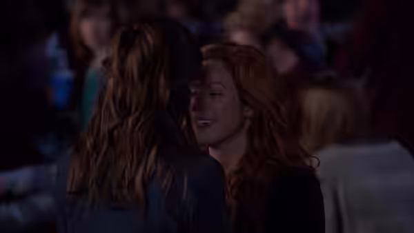 Two women embracing affectionately in a dark auditorium filled with spectators