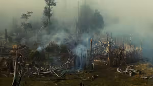 Smoke rises over a burned settlement strewn with fallen timber and bodies
