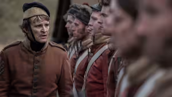 A uniformed officer speaks to a line of red-coated soldiers