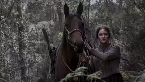 Clare (Aisling Franciosi) stands beside a saddled horse in a forest